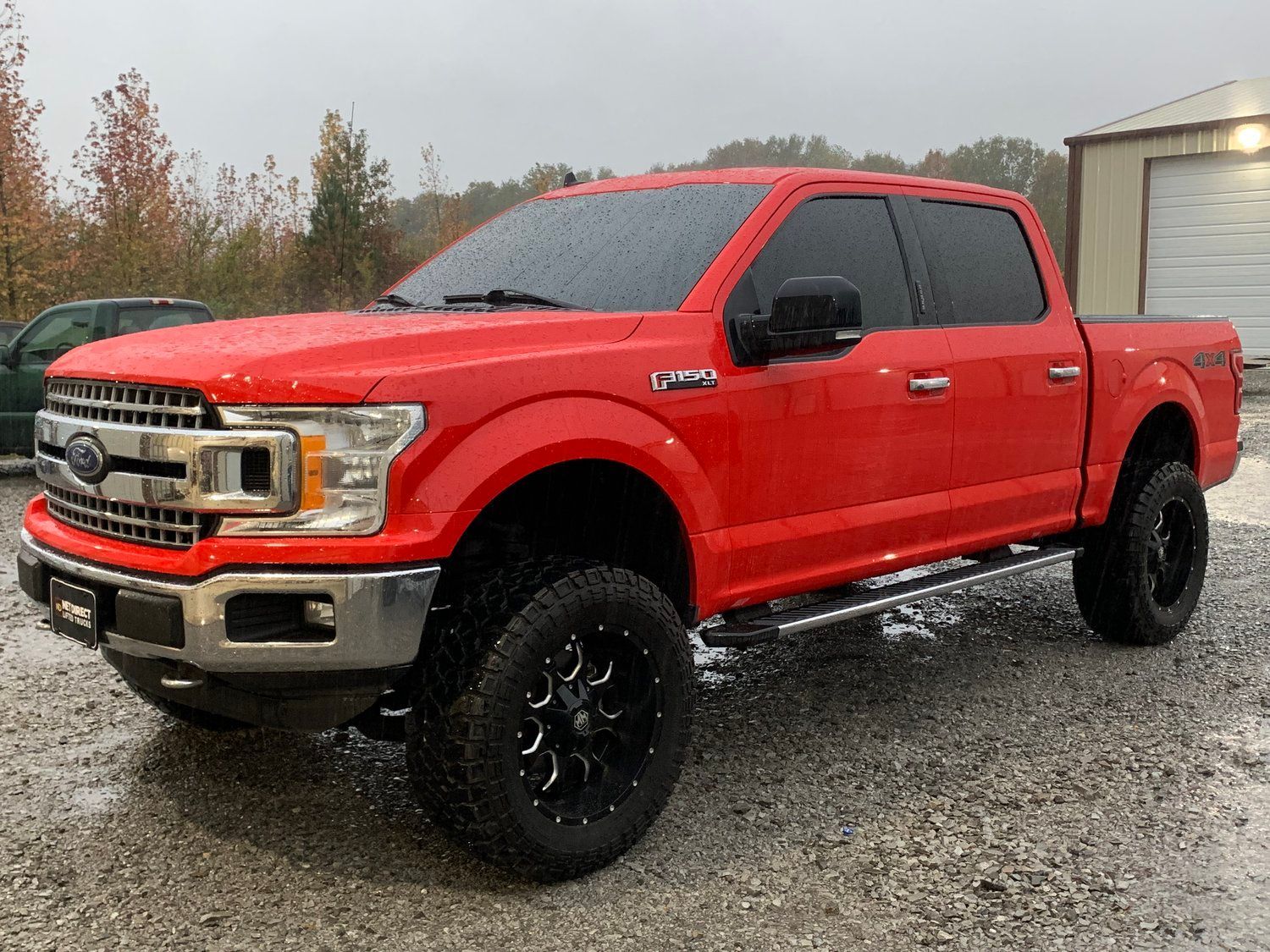 Red Ford F-150 pickup truck with black wheels parked outside on a wet, overcast day.