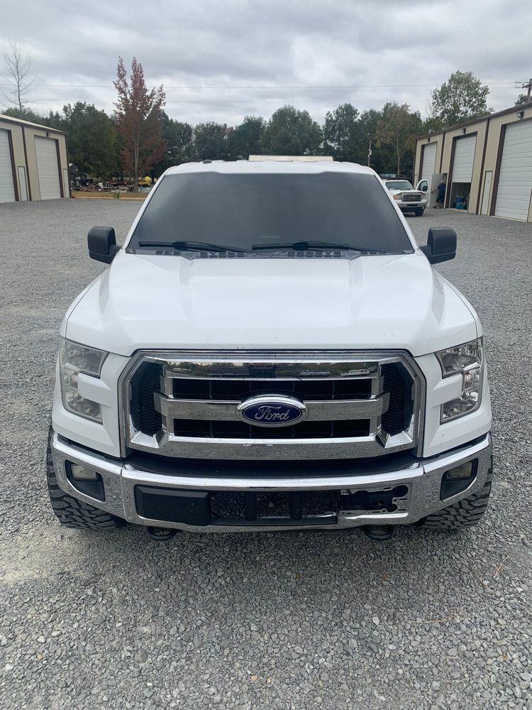 White Ford F-150 truck parked on gravel in front of industrial buildings.