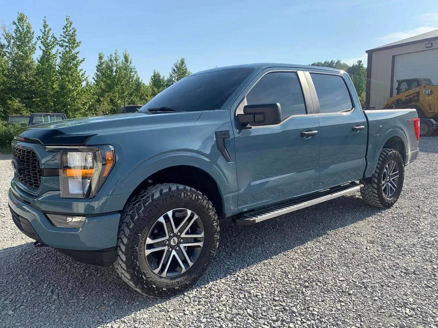 Blue Ford F-150 pickup truck parked on gravel. Blacked-out windows, black grille, and off-road tires.