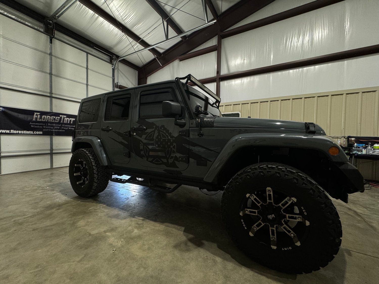 Dark gray Jeep Wrangler with large tires parked in a garage.