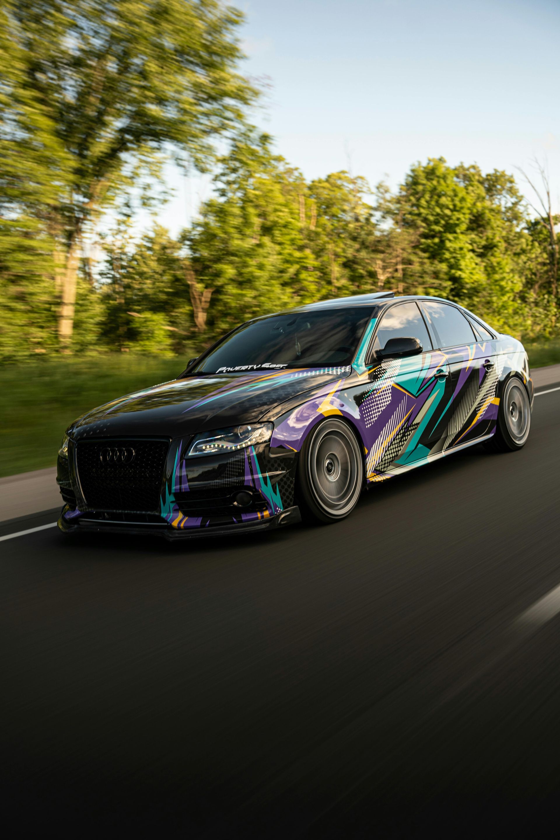 Black Audi sedan with colorful graphics speeding on a road, trees in the background.
