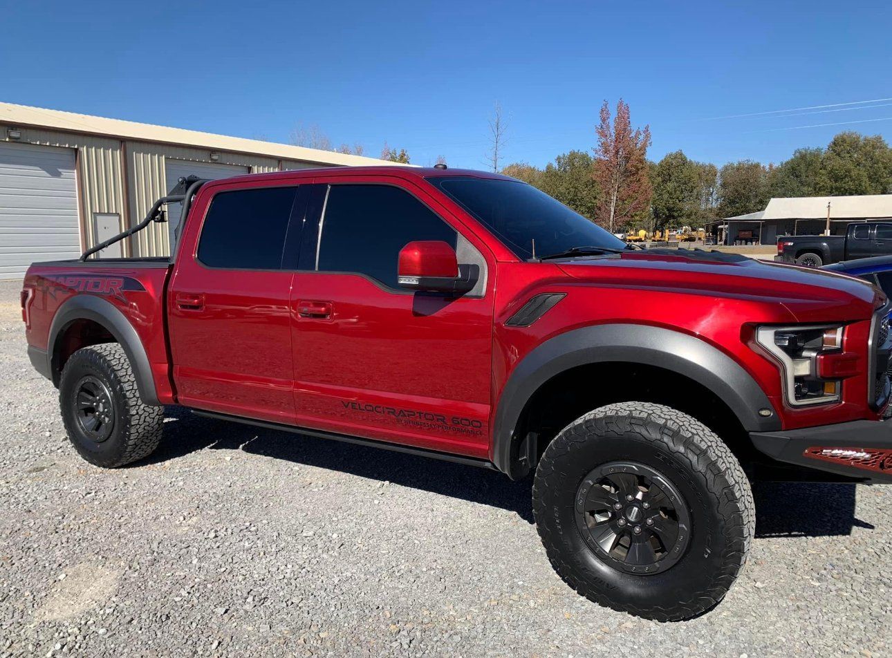 Red Ford Raptor truck with black accents parked on gravel.