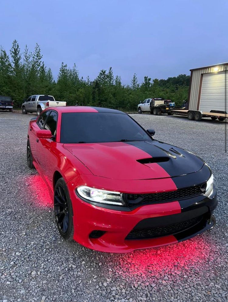 Red and black Dodge Charger with red underglow lights, parked on gravel.