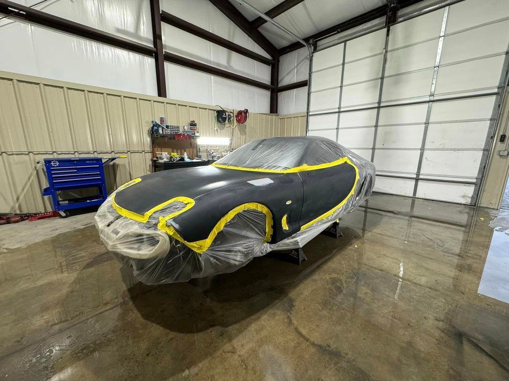 Black sports car partially covered in plastic and yellow tape inside a garage.