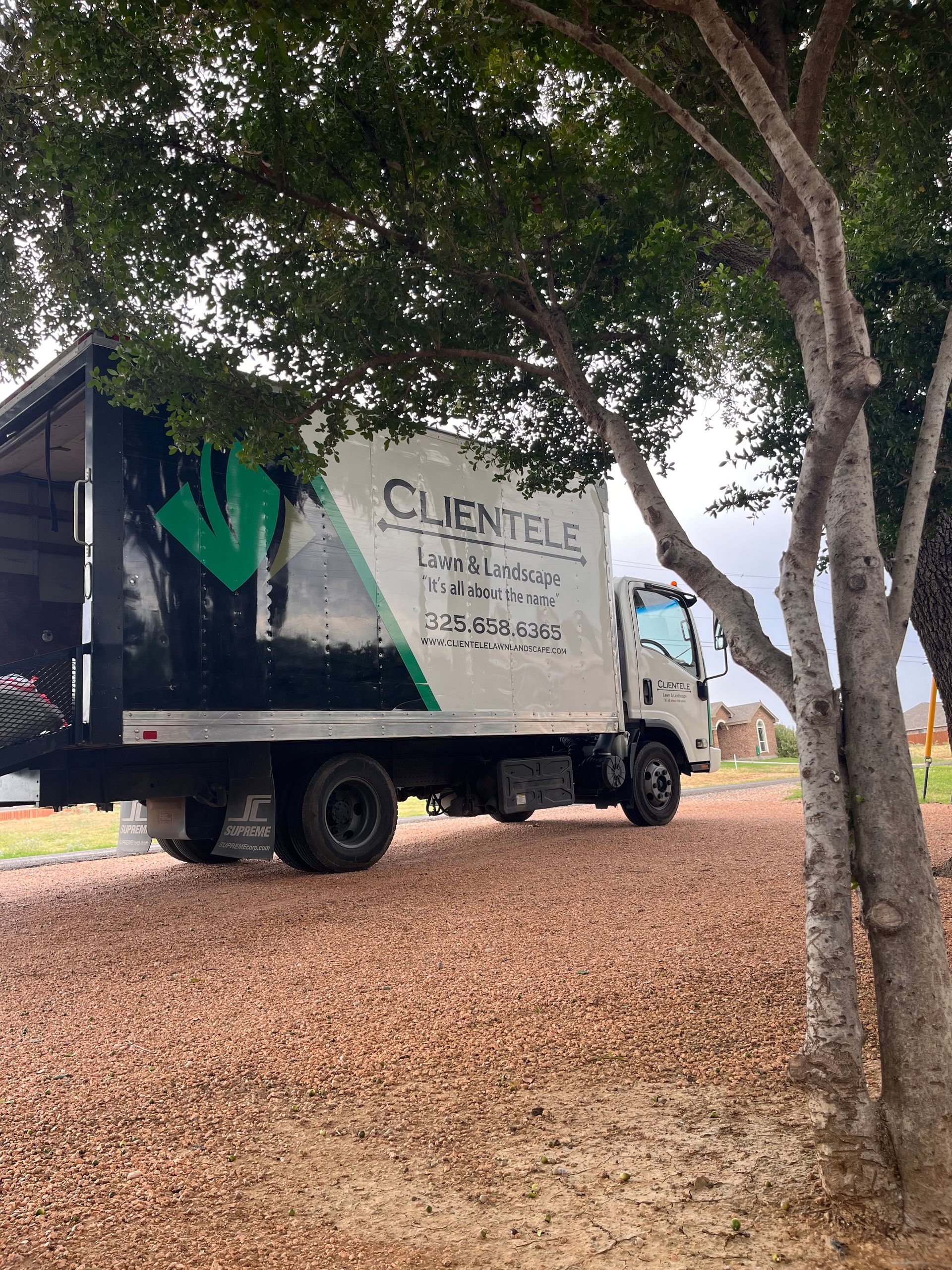 Truck parked on gravel beneath a tree. The truck has green and black logo and text.