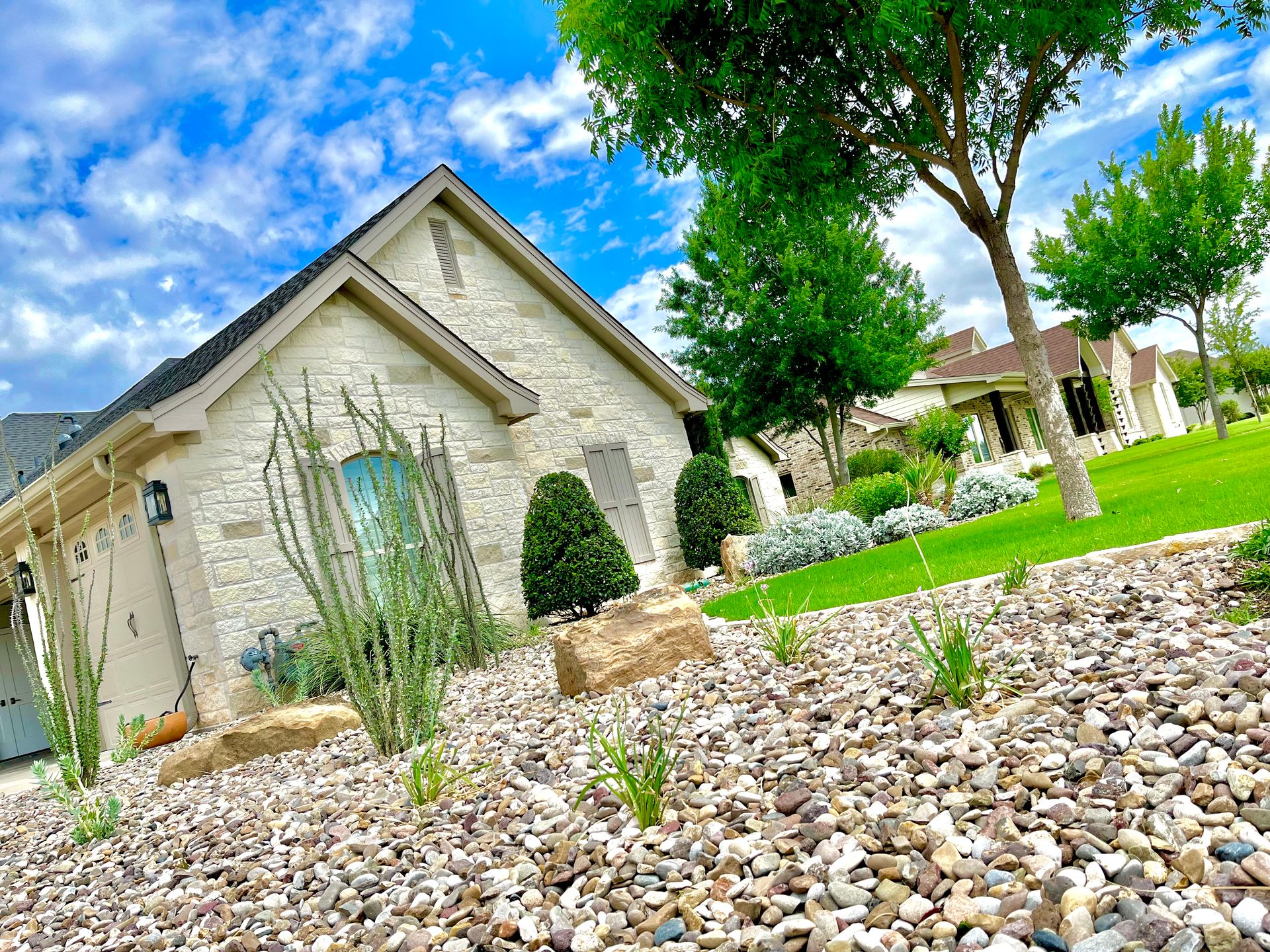 House exterior with tan brick, stone landscaping, and blue sky.