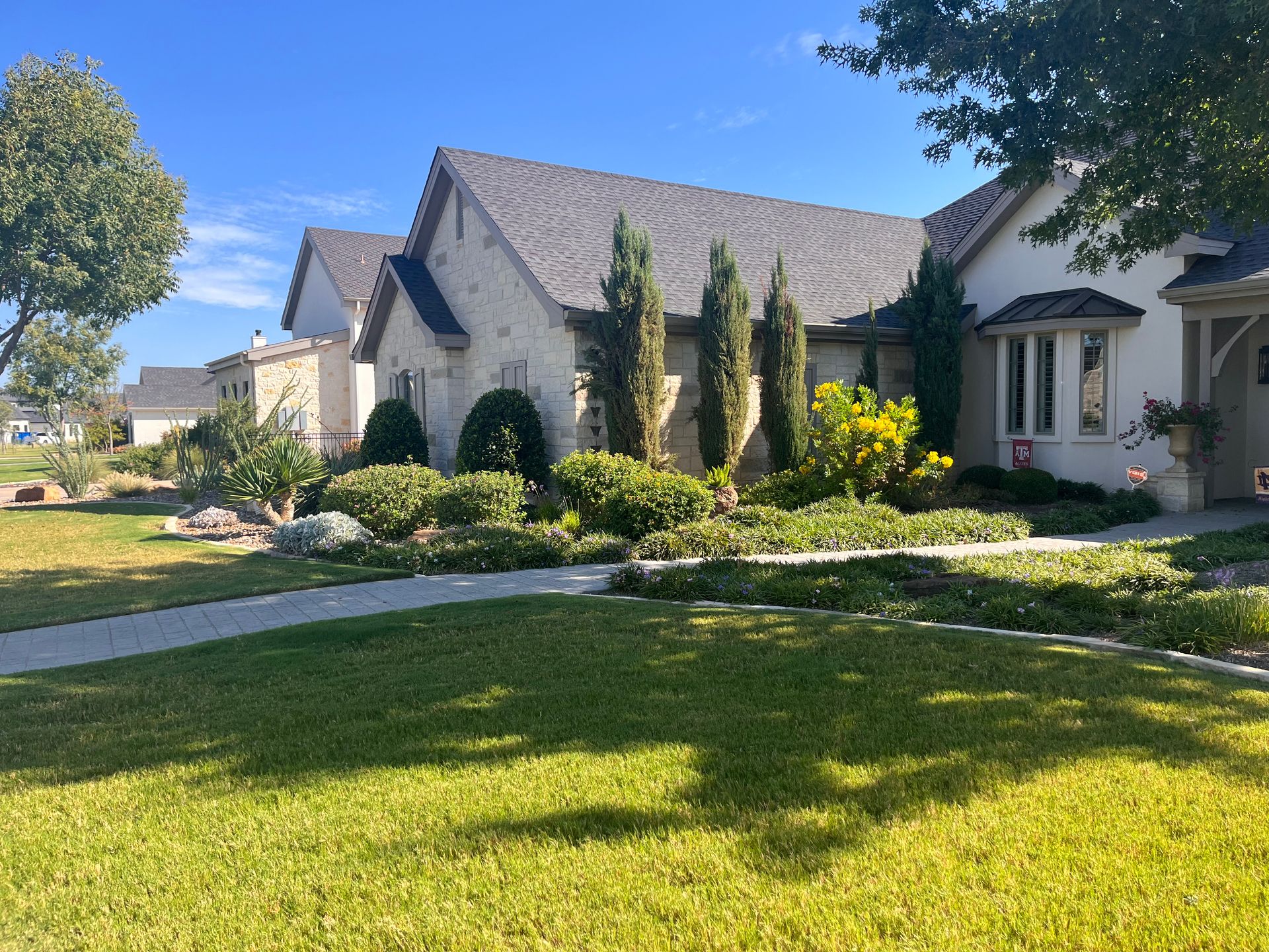 A suburban house with a stone exterior, lush landscaping, and a sunny lawn.