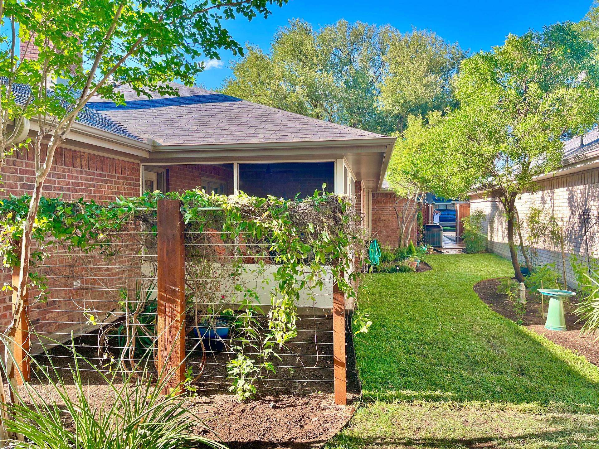 A backyard with a brick house, a vine-covered wall, and a green lawn.