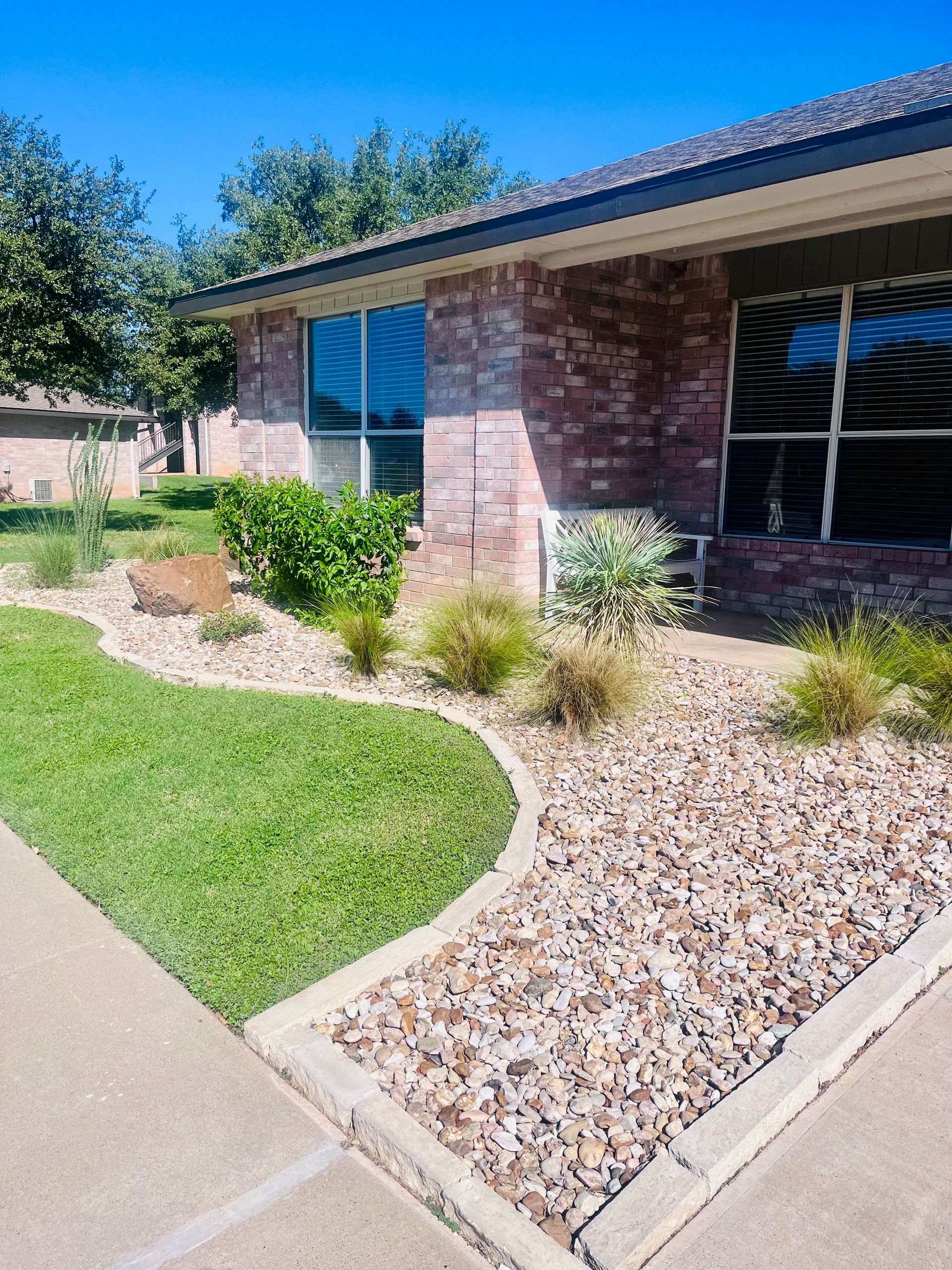Brick house with a rock garden and green lawn under a blue sky.