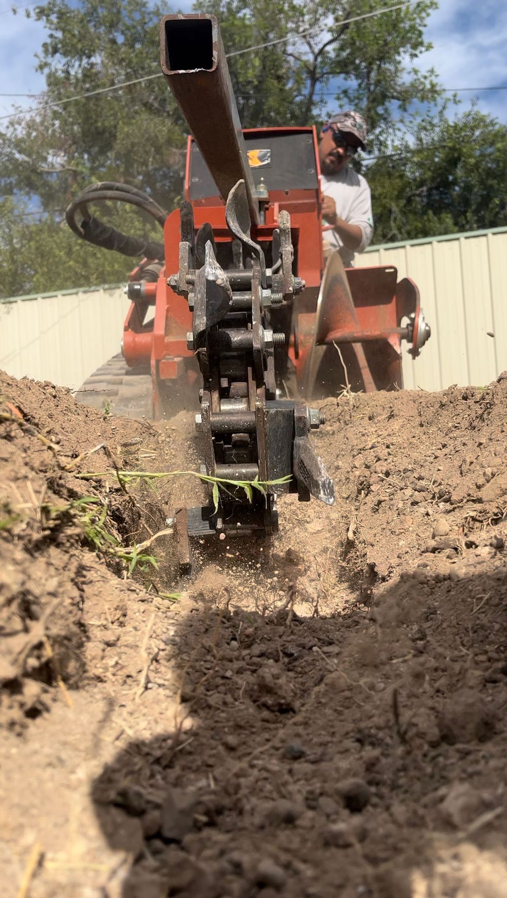 A man operating an orange trencher digging a trench in the dirt outside.