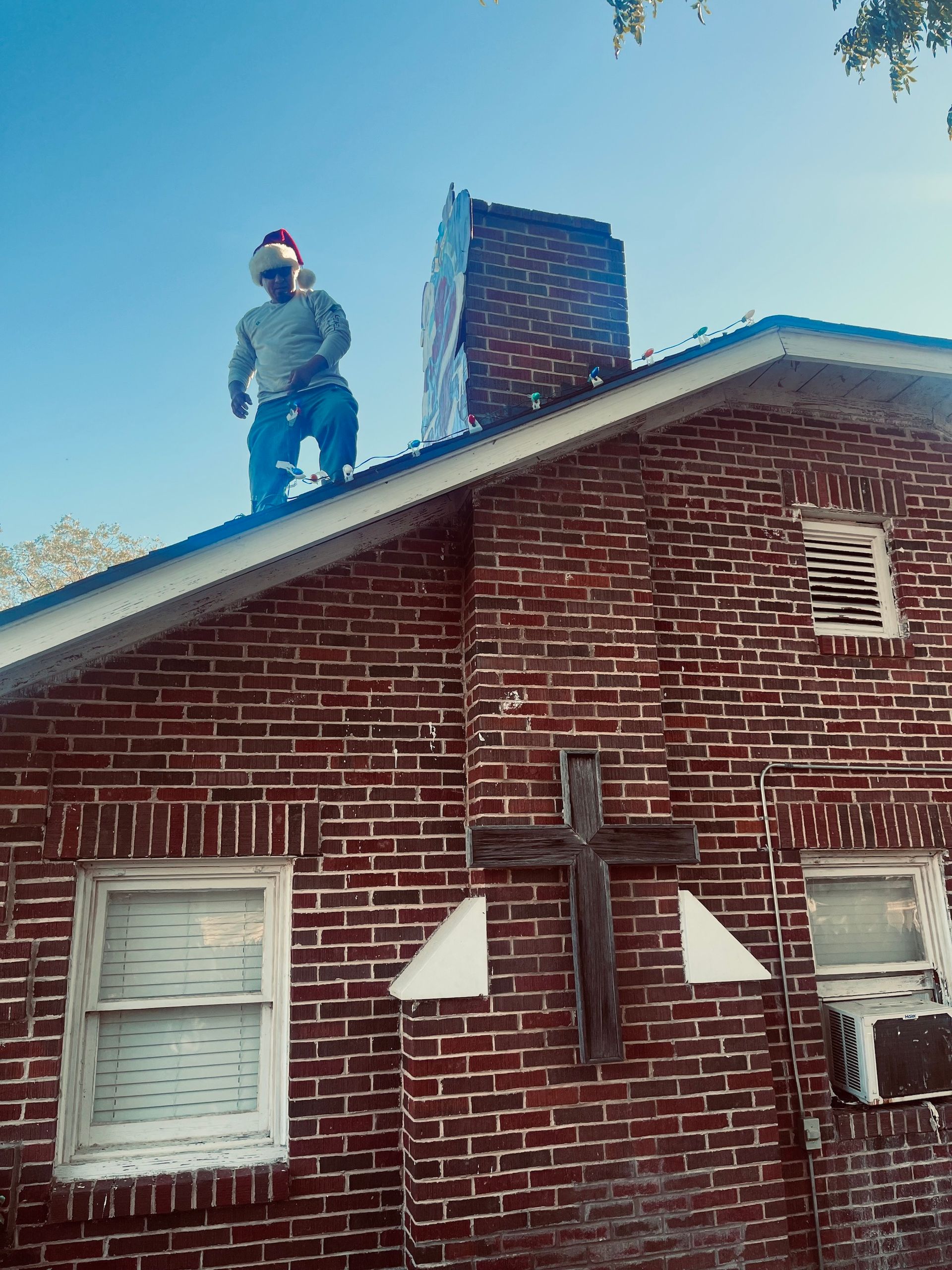 Man in Santa hat on roof; brick building, blue sky.