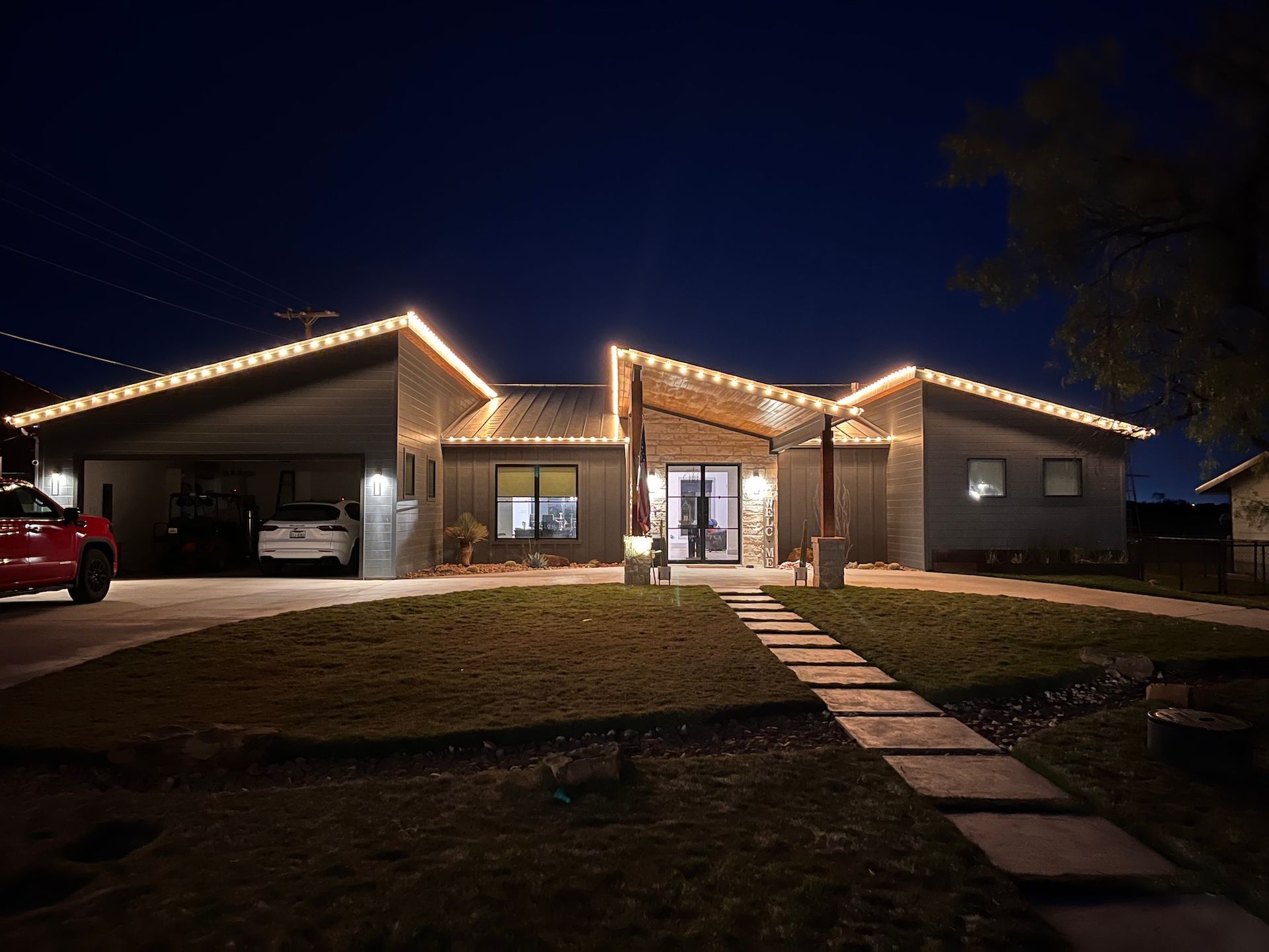 House at night with rooftop lights, a car in the driveway, and a stone path leading to the entrance.