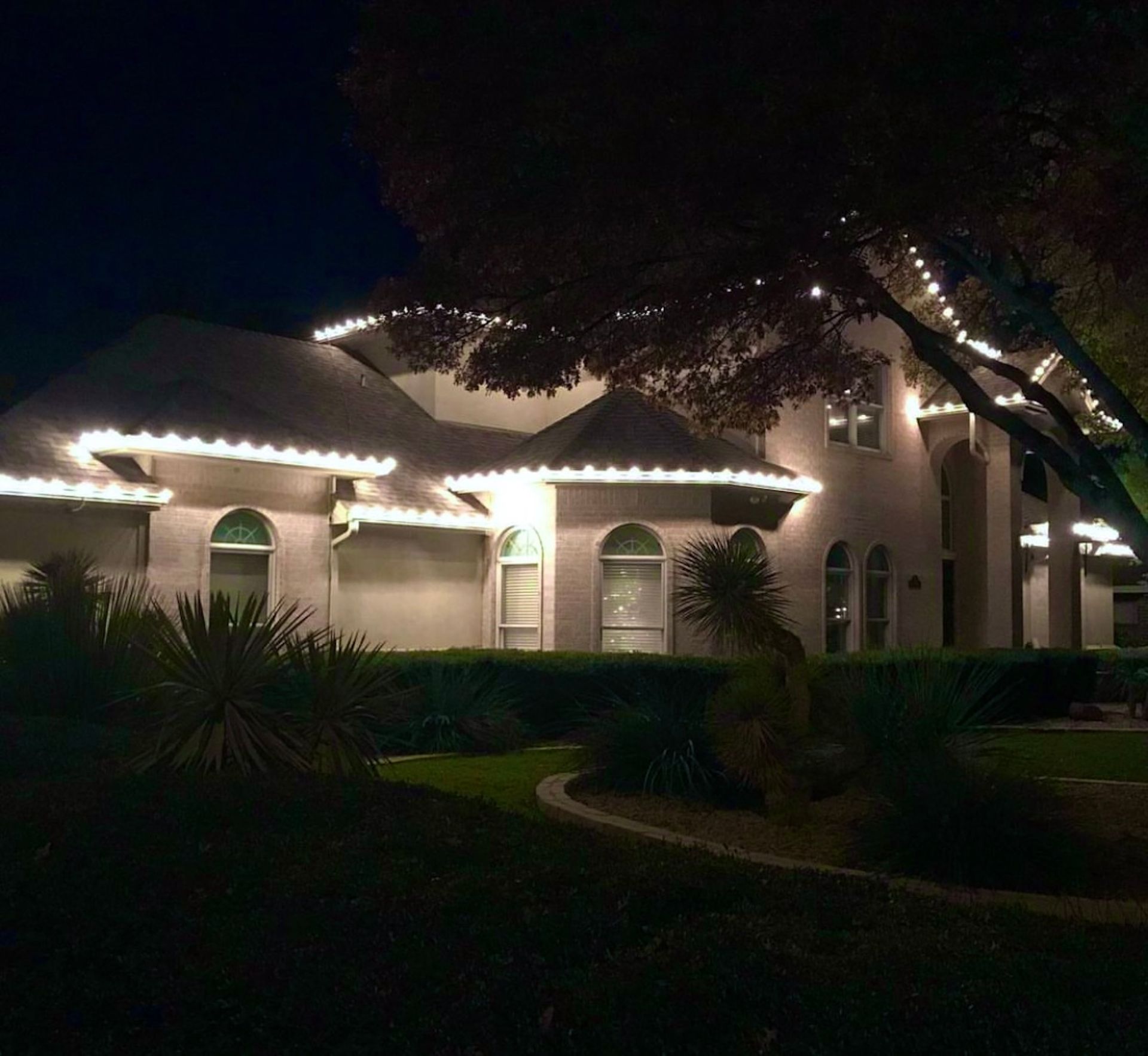 House at night, lit with white lights along rooflines and trees.