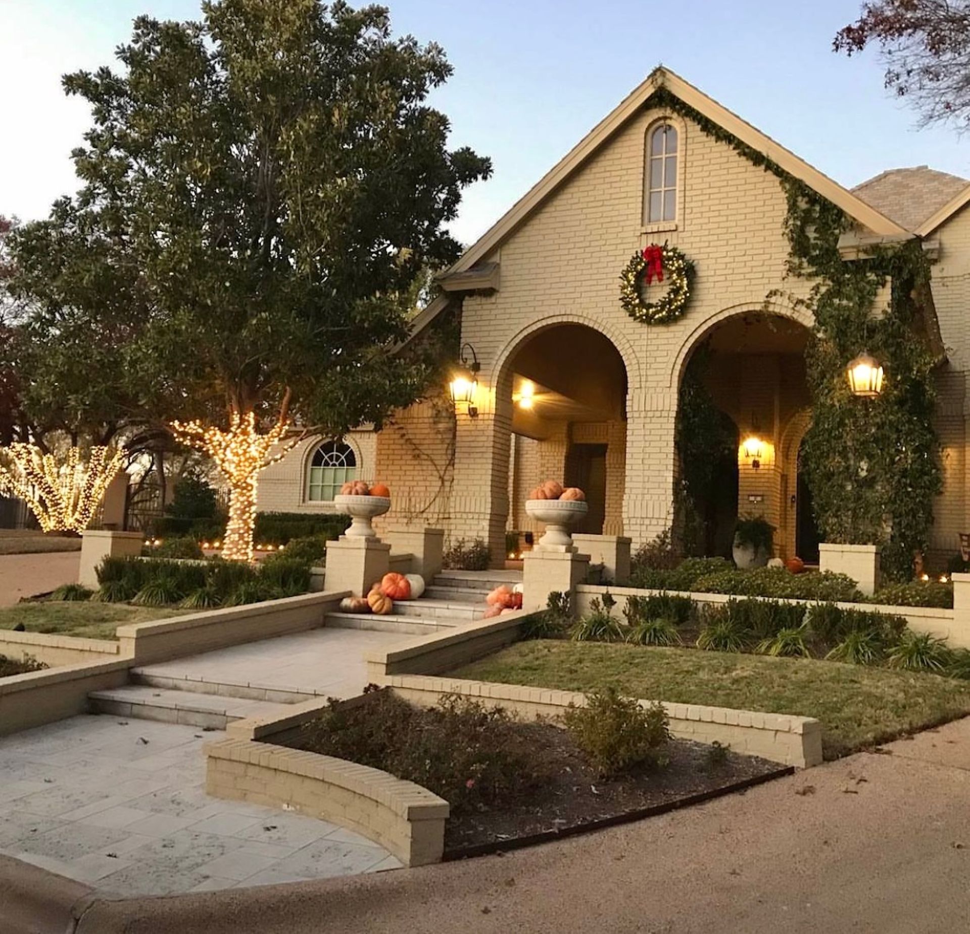 Cozy house decorated for fall with pumpkins and a wreath. Lit tree and climbing vines.