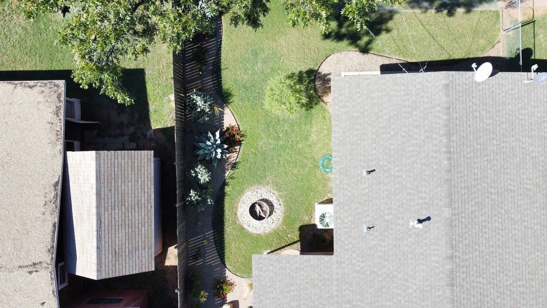 Overhead view of two houses, a narrow yard with green grass, trees, and a fire pit.