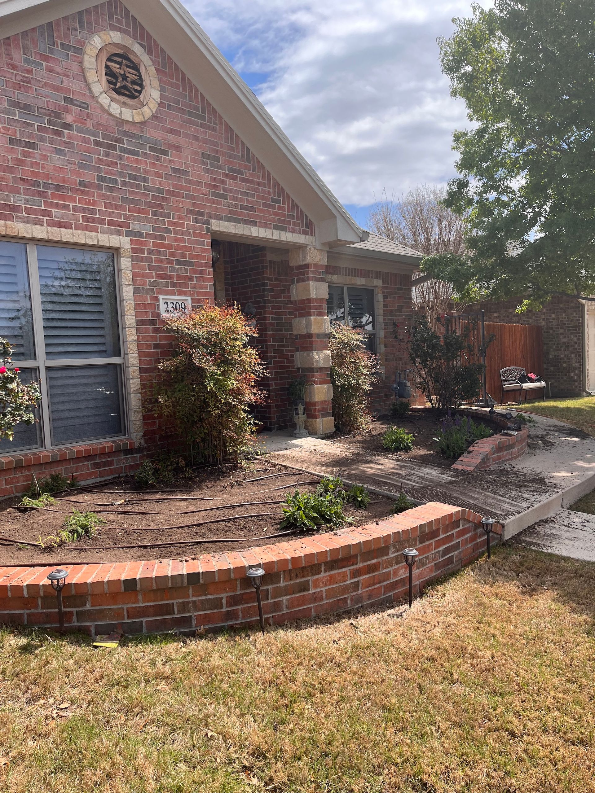Brick house with flower beds and a brick retaining wall; lawn in the foreground.