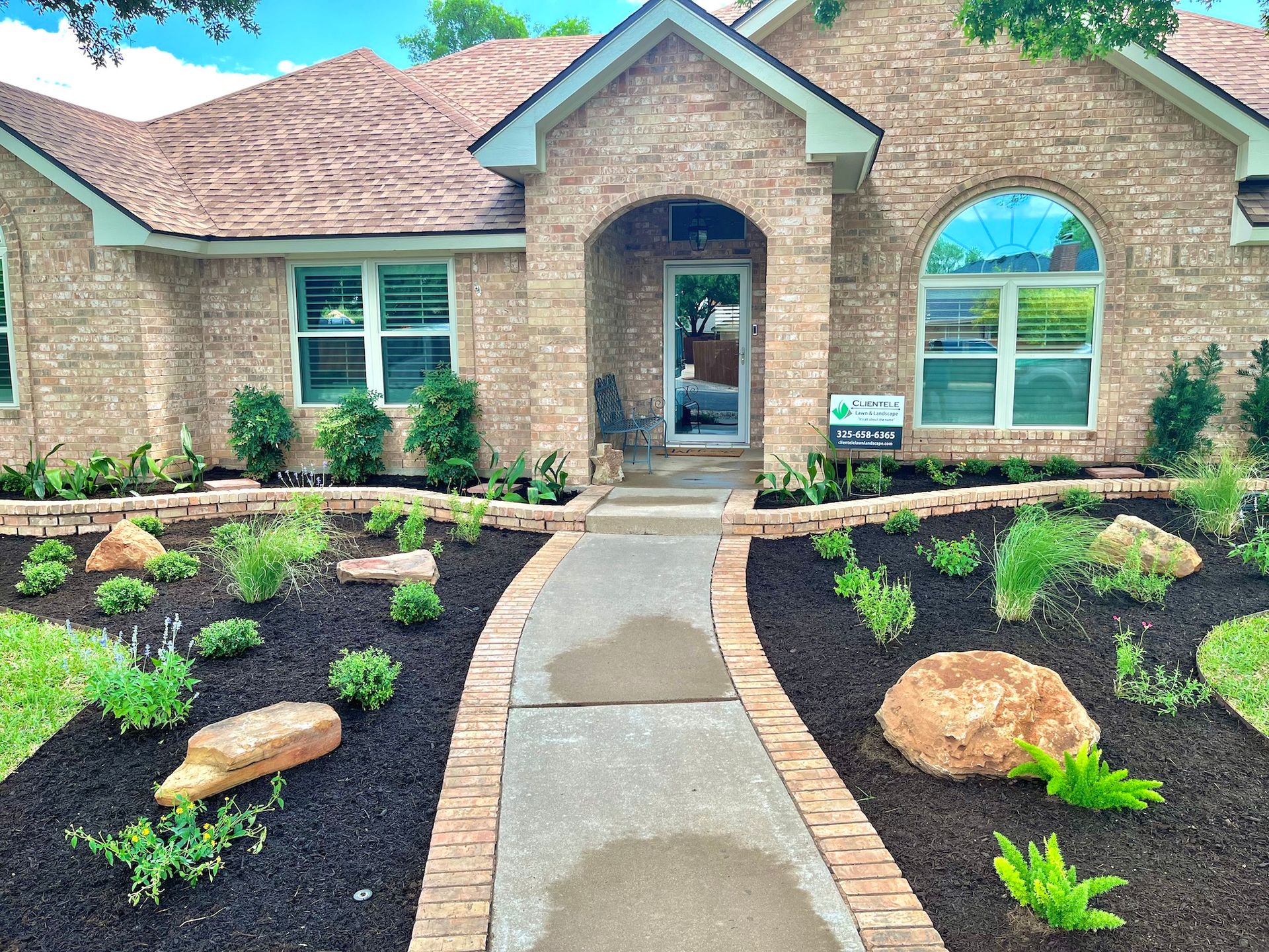 Brick house with landscaped front yard, walkway, and colorful mulch.