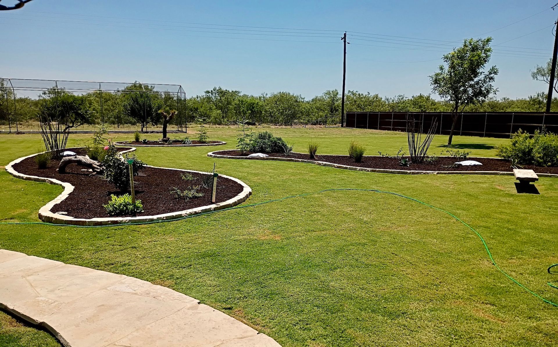 Well-maintained yard with flower beds, a curved sidewalk, and a clear blue sky.