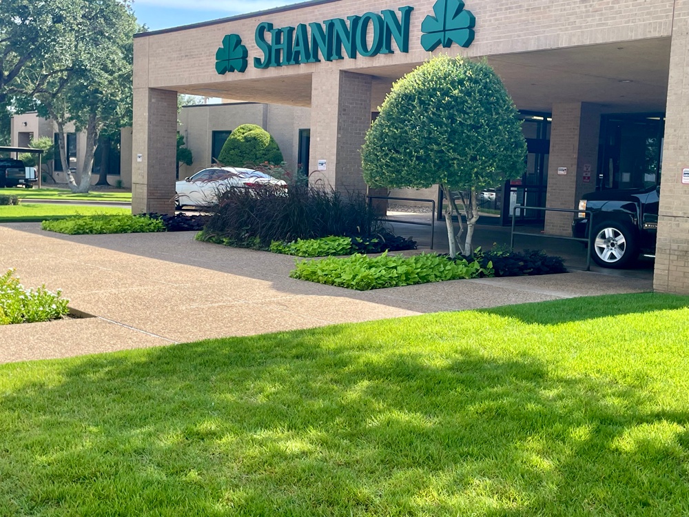 Shannon hospital entrance with a car parked under the portico. Green landscaping and a sign.