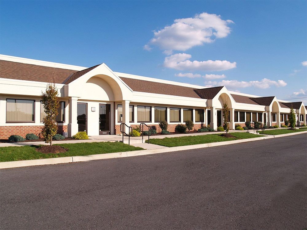 Office building with multiple entrances, tan roof, brick and white accents, blue sky.