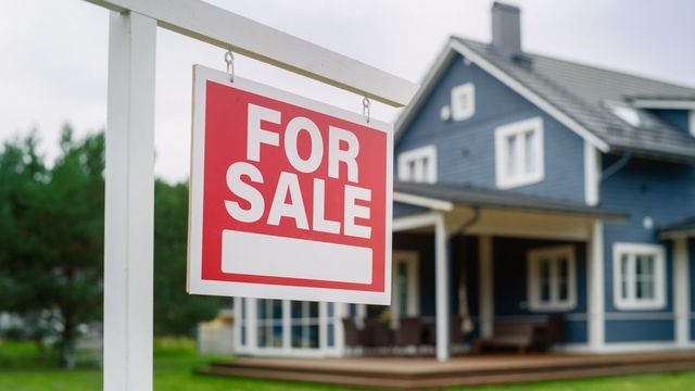 A for sale sign is hanging in front of a blue house.