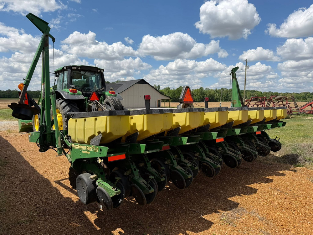Green and yellow tractor planter in a field under a cloudy blue sky