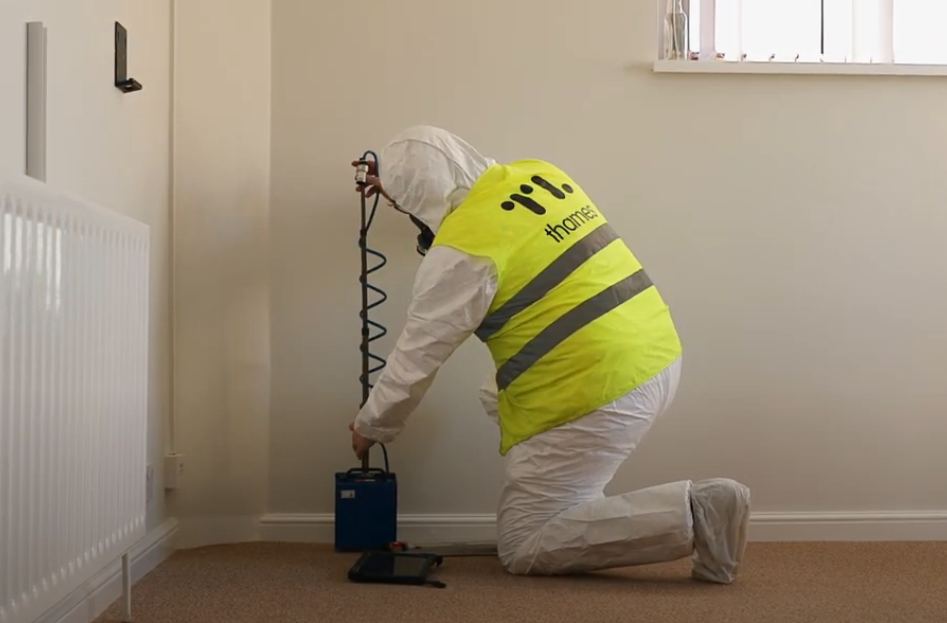 A man in a yellow hi-vis vest is kneeling down in a room with air testing equipment.