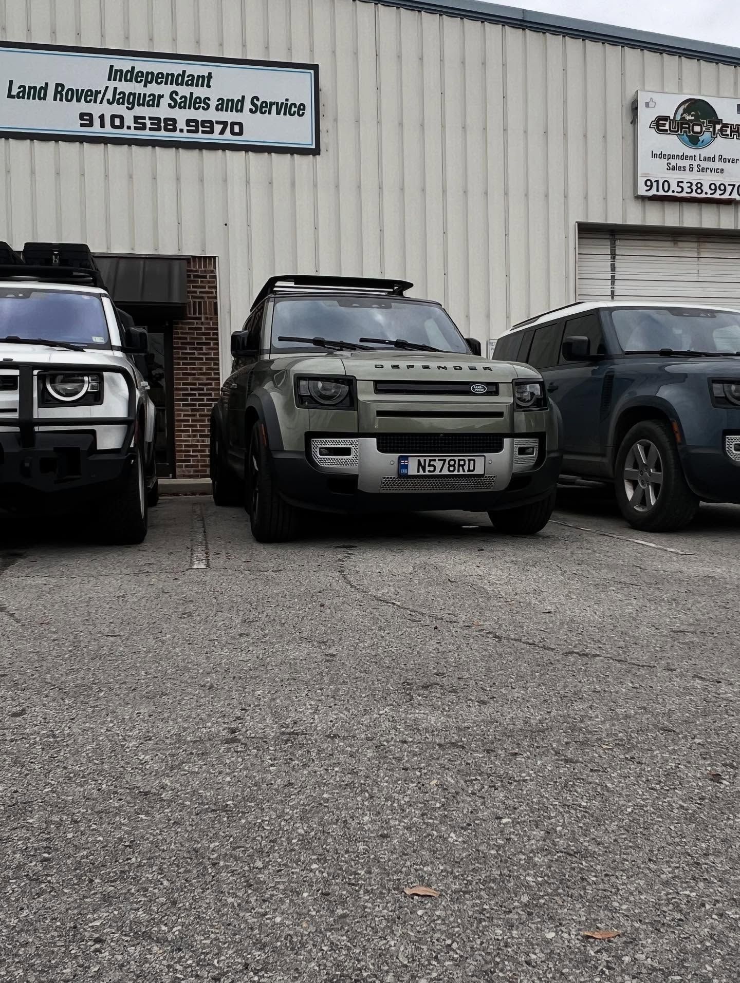 Three Land Rover Defenders parked in front of a building with a sign that says