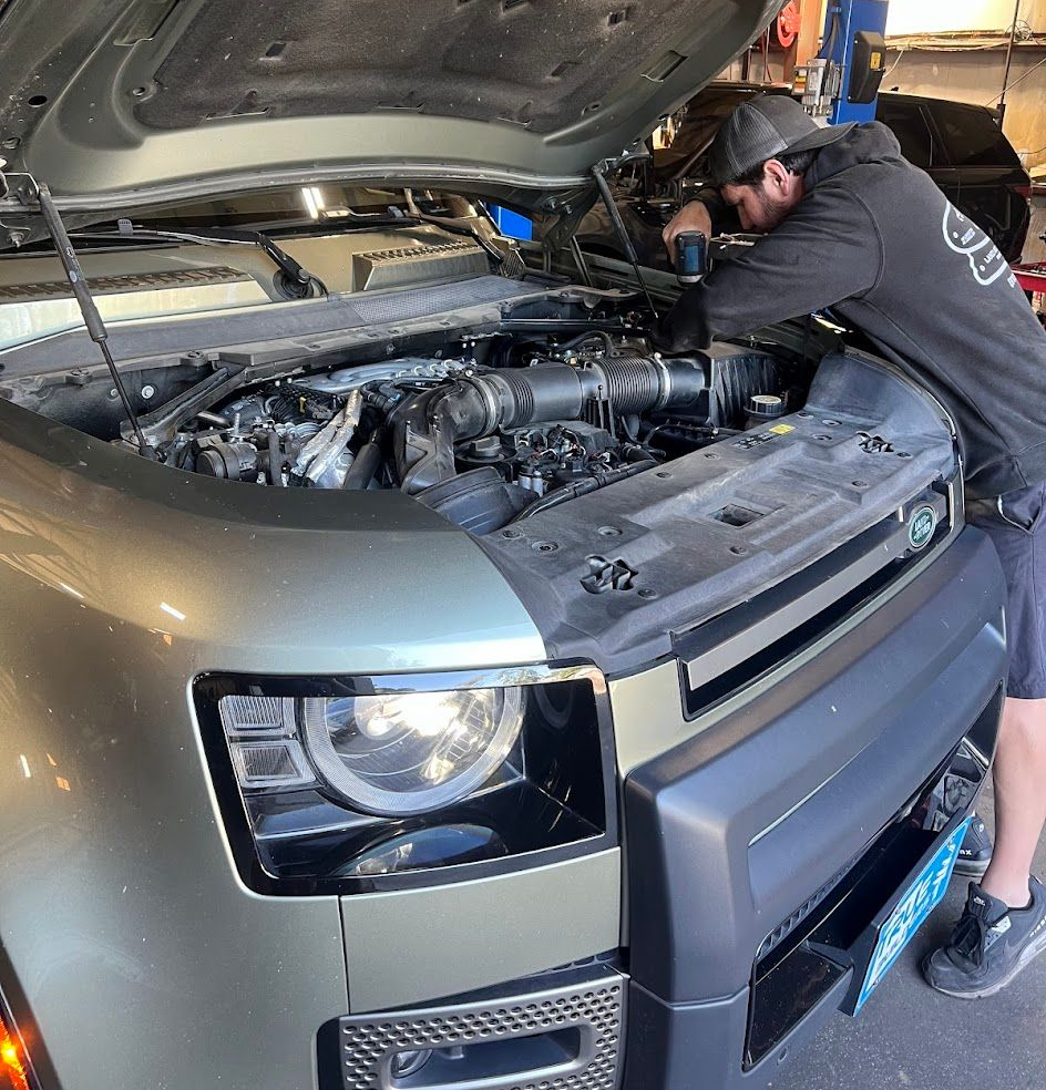 Mechanic working under the hood of a Land Rover SUV with the hood open in a garage in Wilmington, NC.