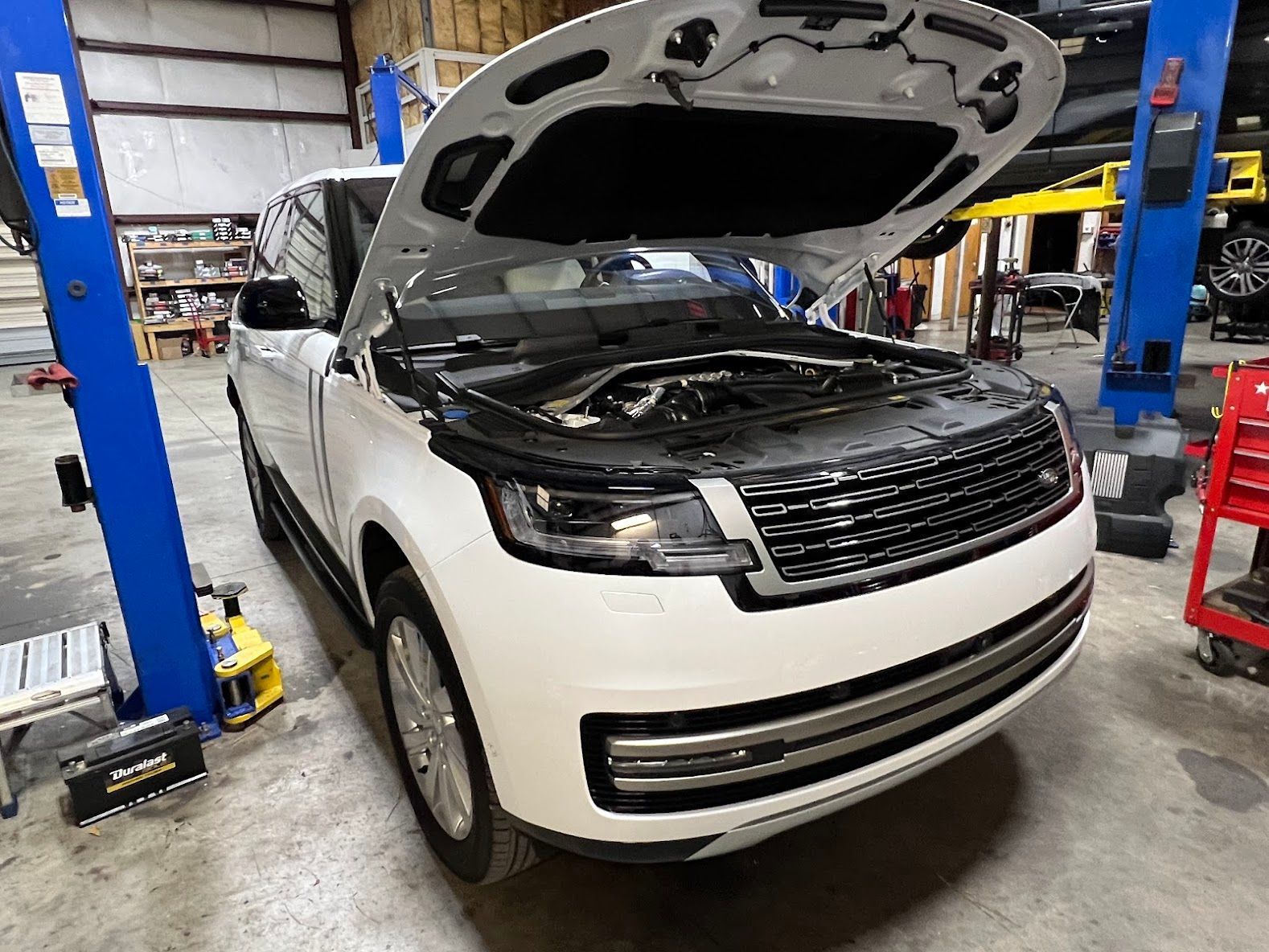 White SUV with hood open in an auto repair shop lift bay