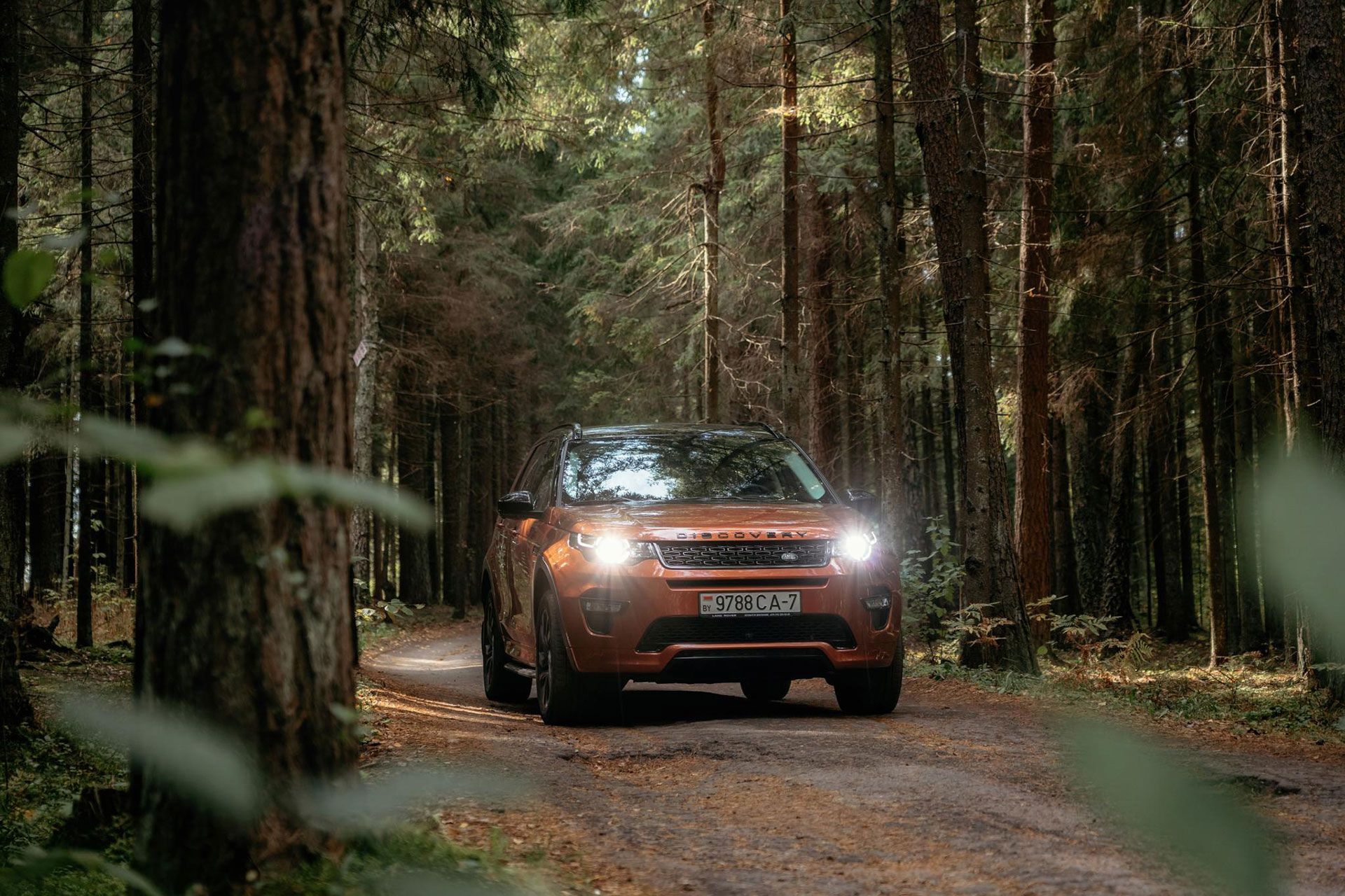 A car is driving down a dirt road in the woods.