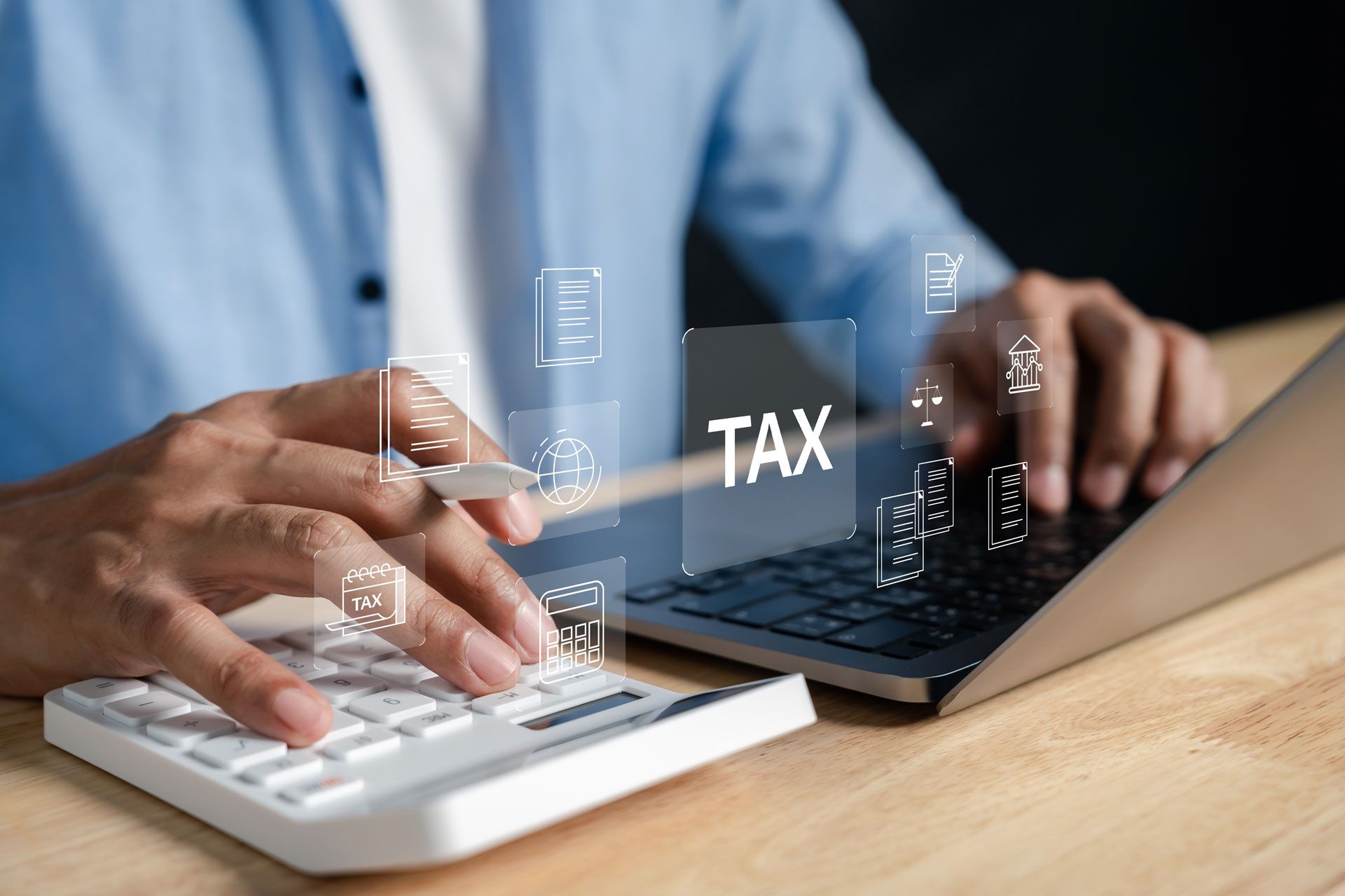 Person calculating taxes on a calculator next to a laptop; digital 