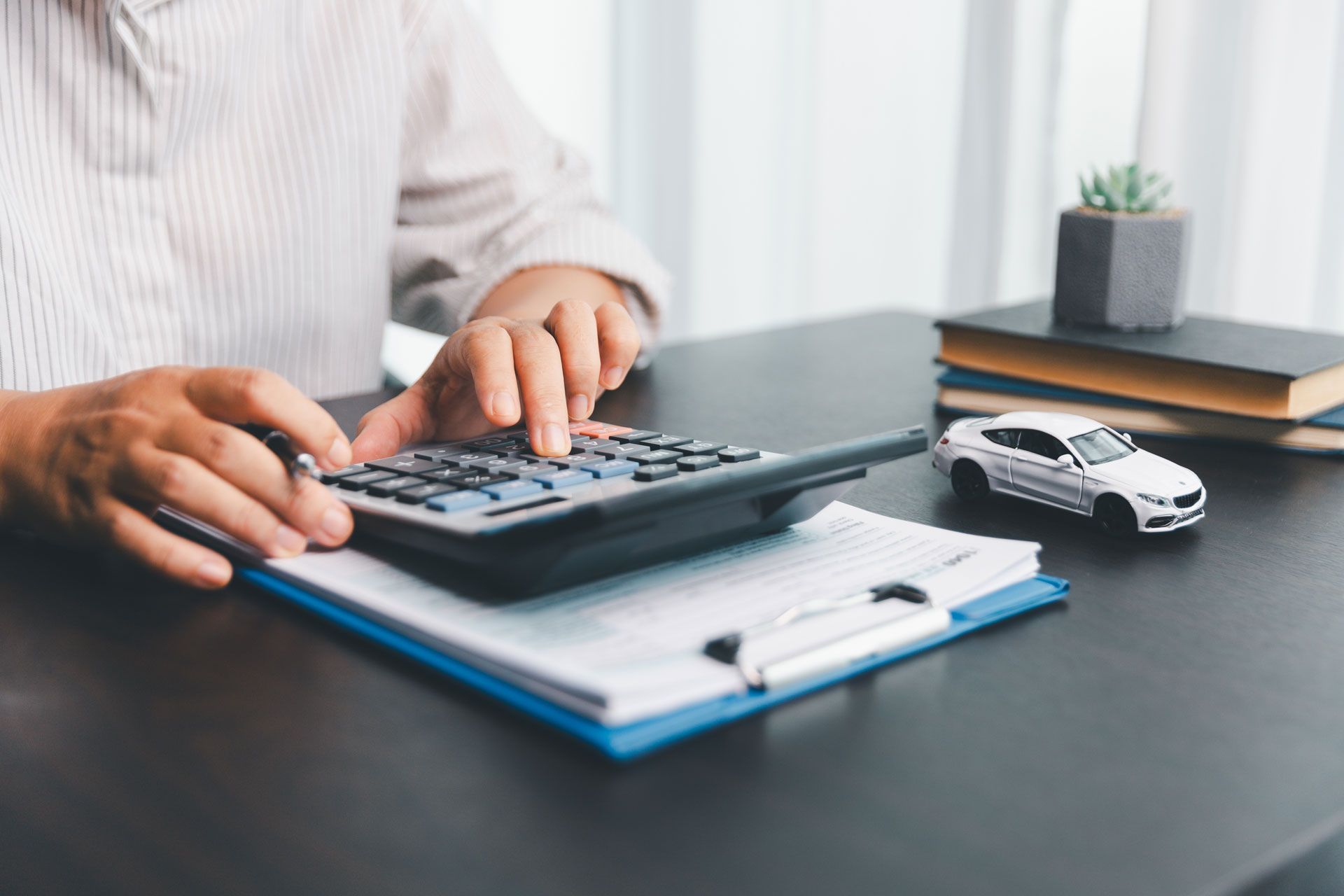 Person calculating car costs with calculator, paper, and toy car.