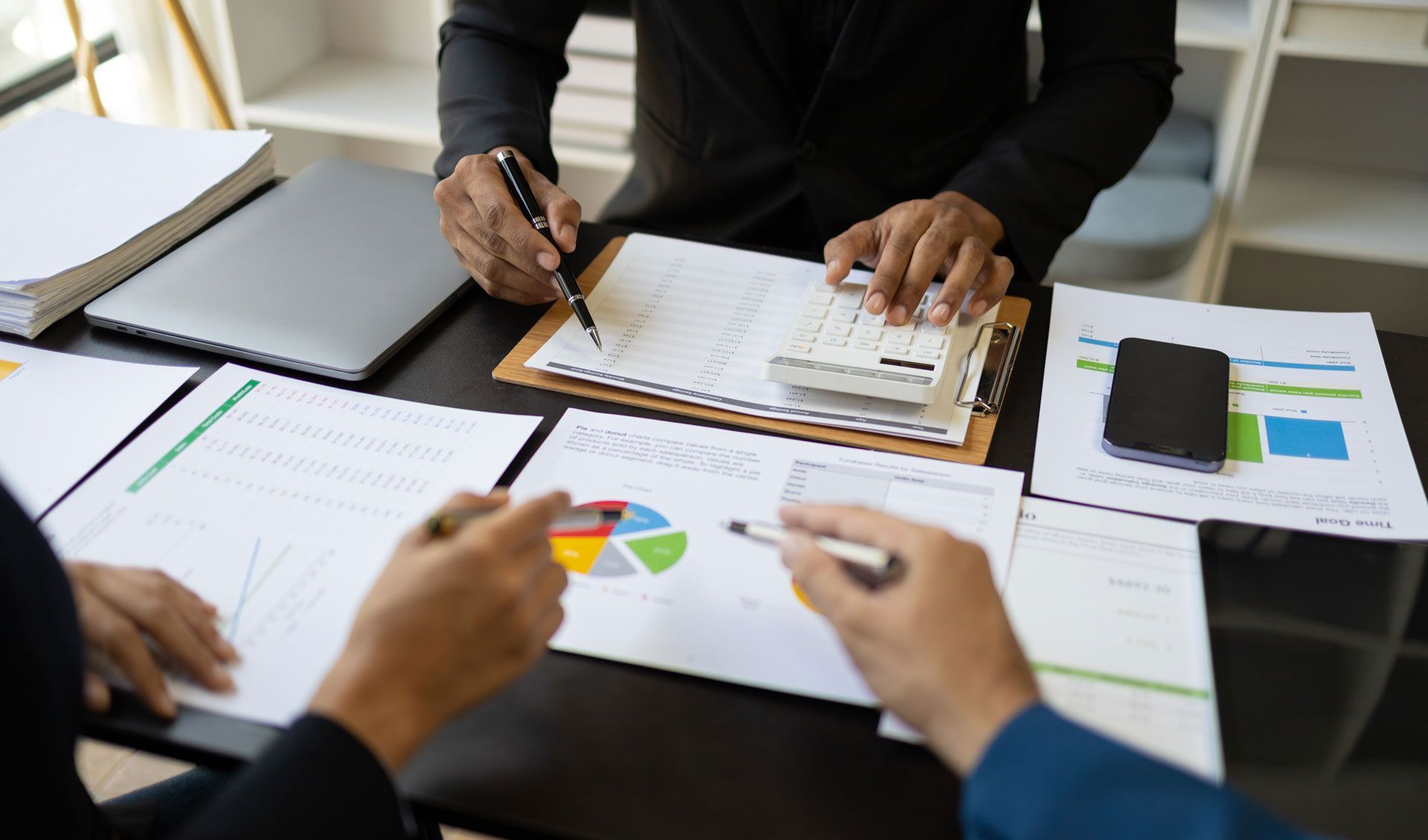 People reviewing financial reports at a desk, with documents, calculator, and pie chart.