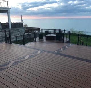 Wooden deck overlooking the ocean at sunset, with black railing and a fire pit.