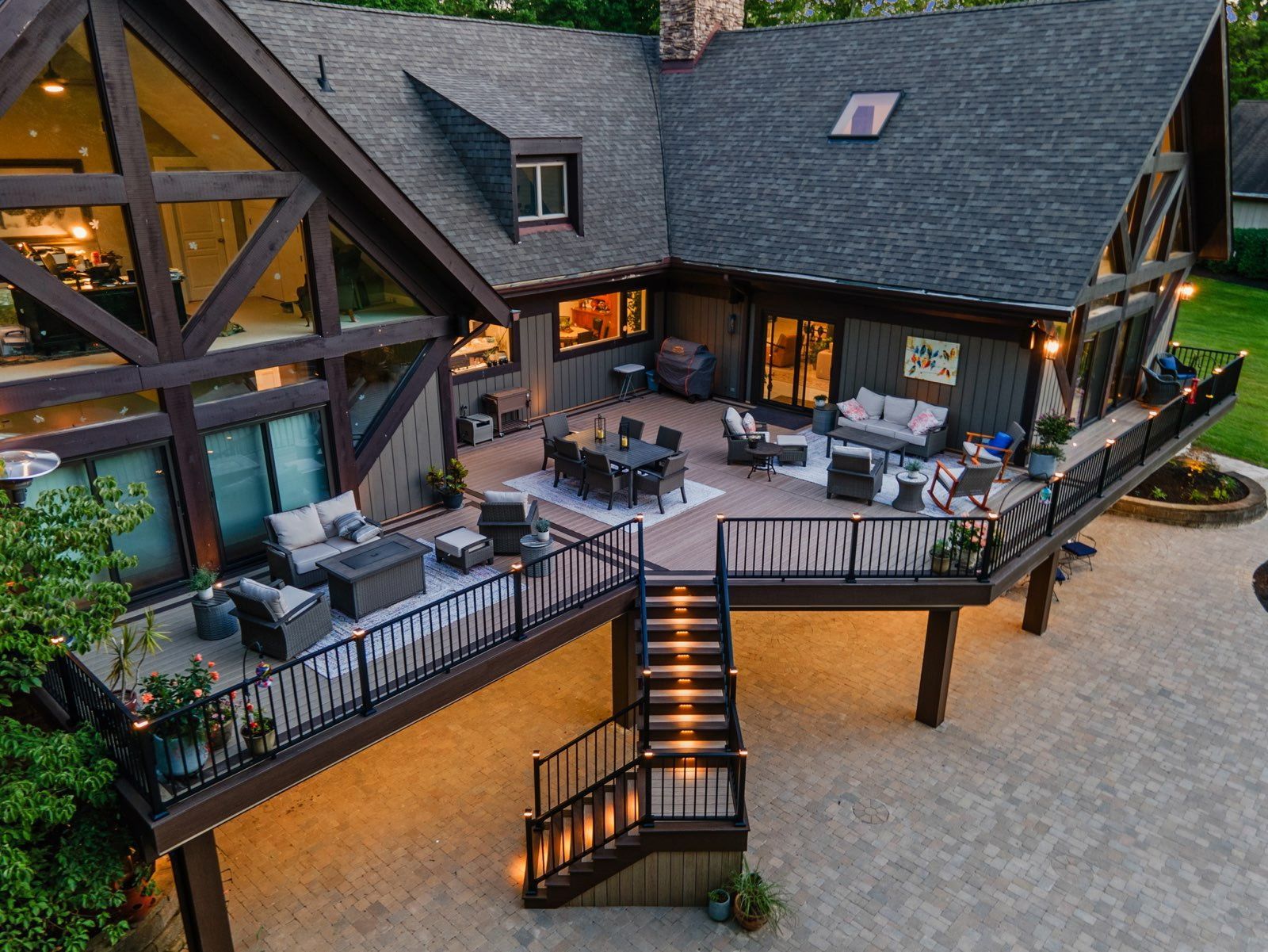 Outdoor deck with lounge seating and string lights around a large house at dusk
