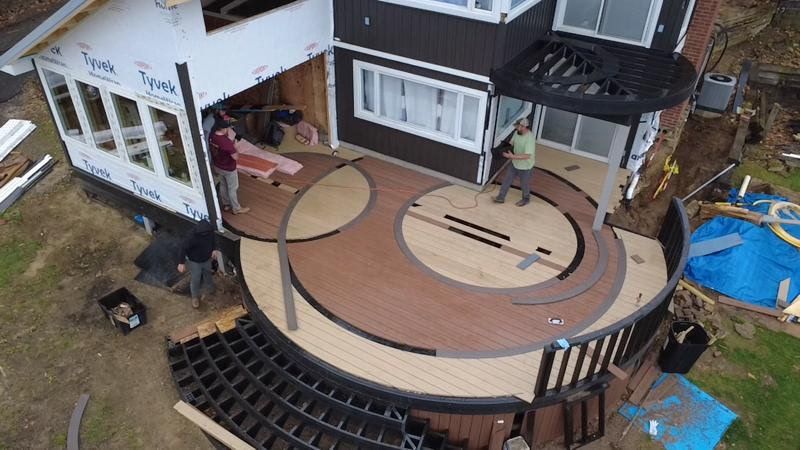 Aerial view of a house deck under construction with curved wooden flooring and black framing.