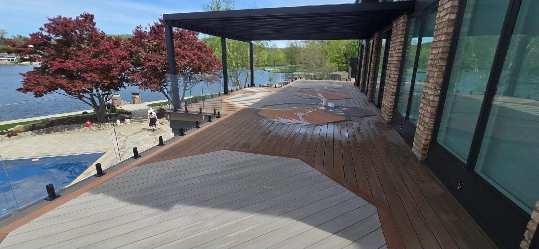 Covered seaside walkway with wooden deck, glass wall, and red tree overlooking the water