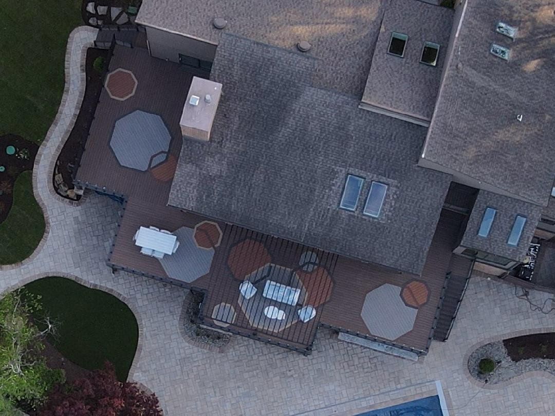 Aerial view of a house patio with outdoor table, chairs, and umbrellas on a stone terrace.