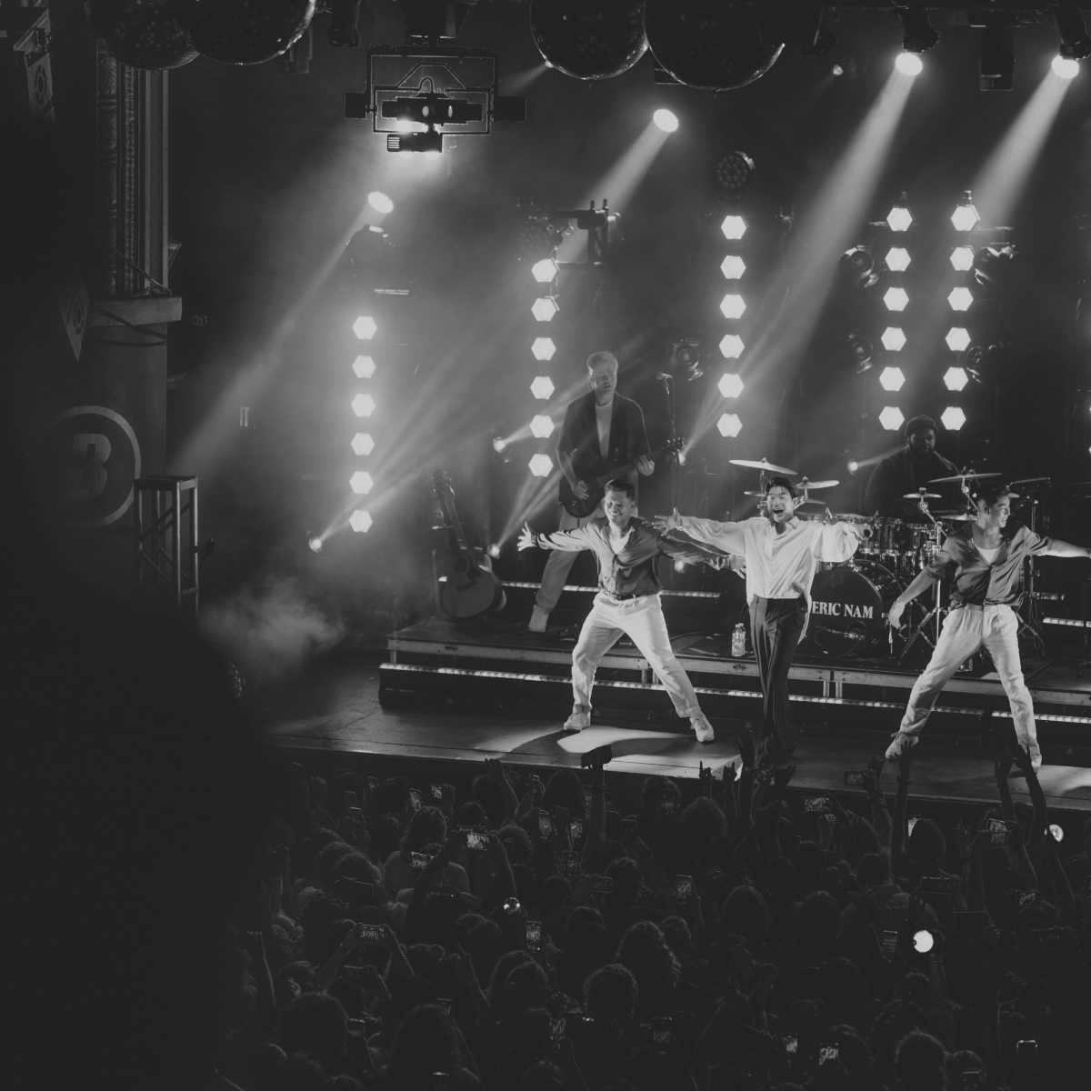 Band performing on stage with spotlights and a crowd.
