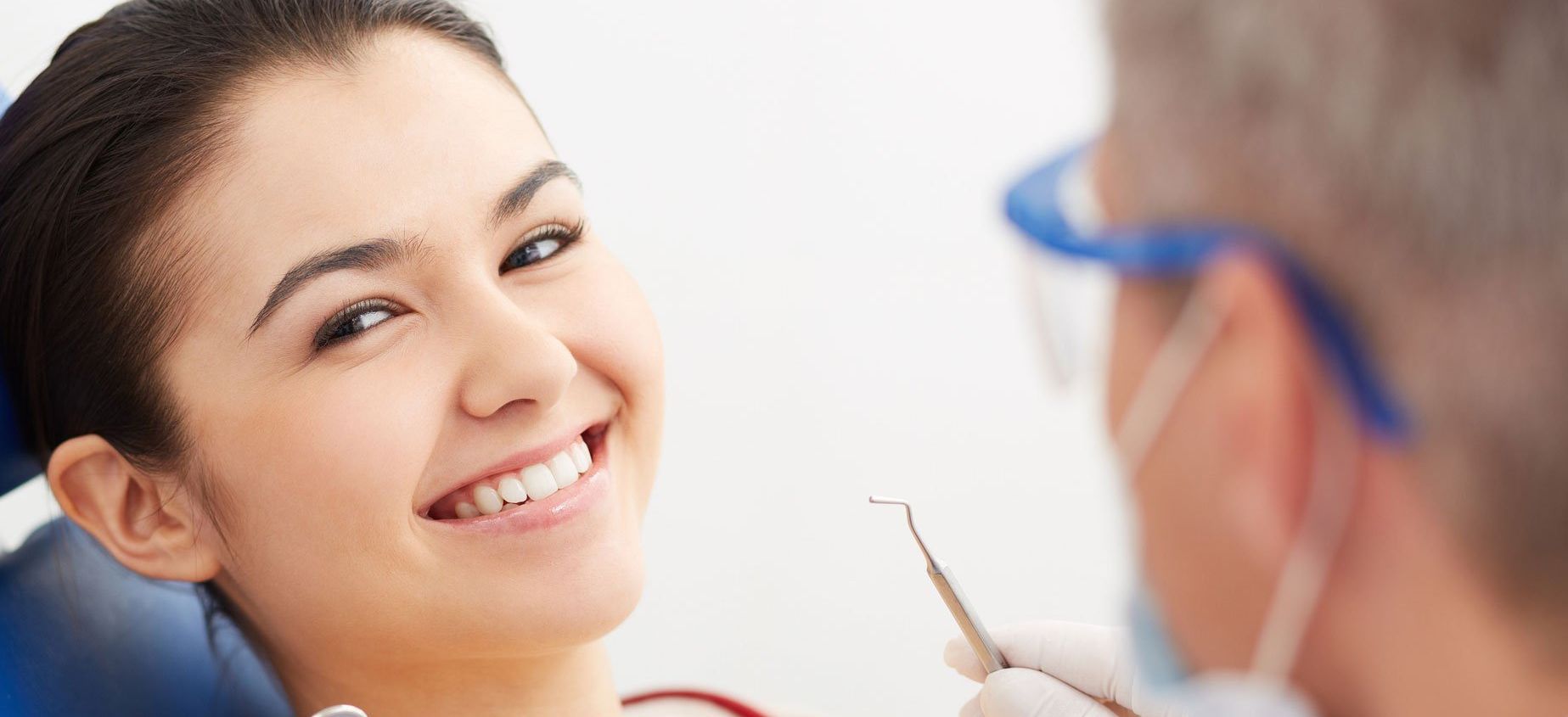 A woman is smiling while having her teeth examined by a dentist.