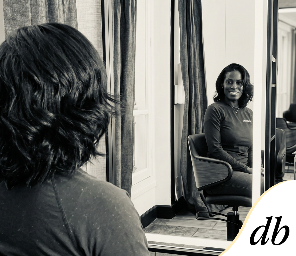 Une personne aux cheveux courts, foncés et ondulés contemple son reflet souriant dans le miroir d'un salon de coiffure.
