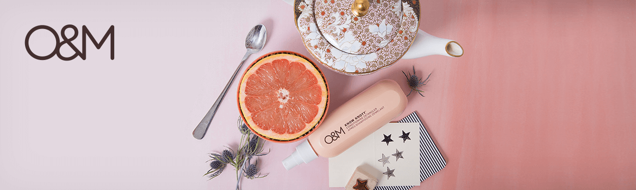 Une tranche de pamplemousse, une théière, une cuillère et un tube de produit sur fond rose.