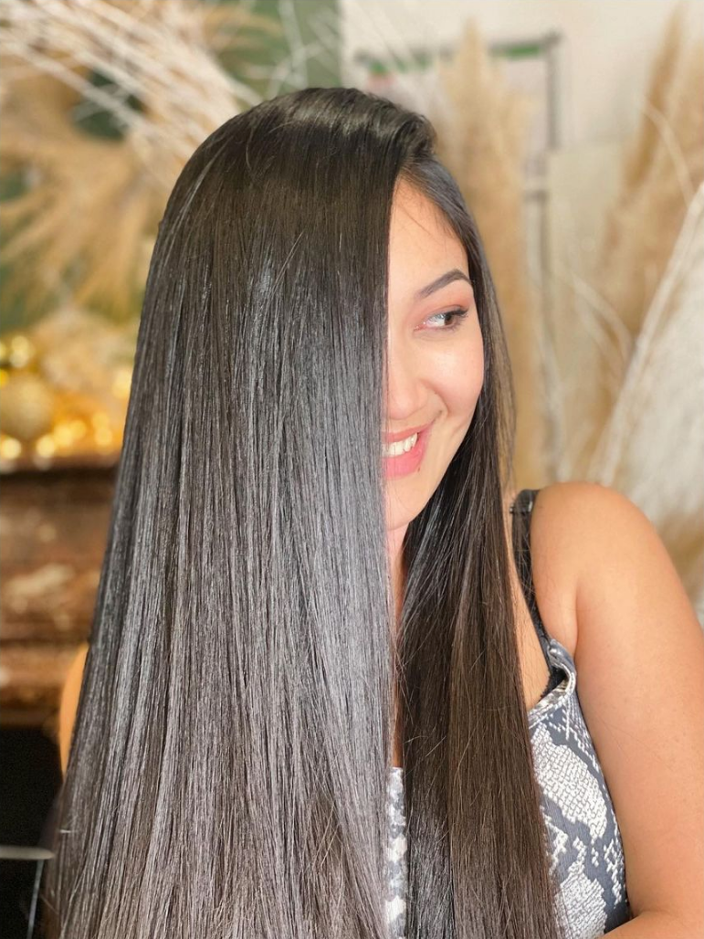 Femme aux longs cheveux noirs ondulés, souriante et regardant vers la droite, portant un haut à motifs.