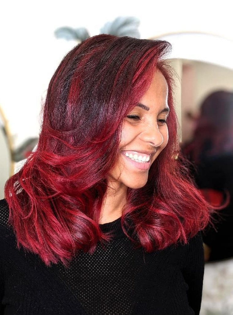 Une femme aux cheveux roux foncé mi-longs affiche un large sourire.