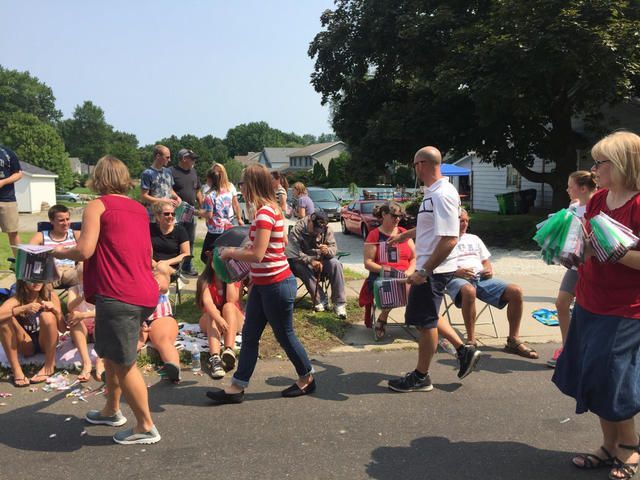 People walking and dancing outdoors at a community event on a sunny street.