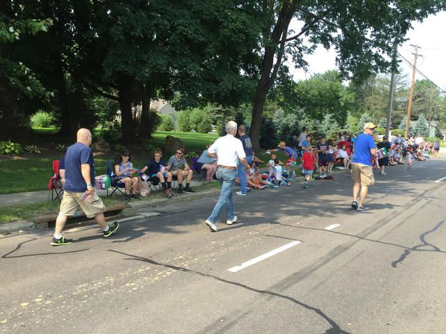 People seated along a tree-lined road as volunteers walk past during a community parade
