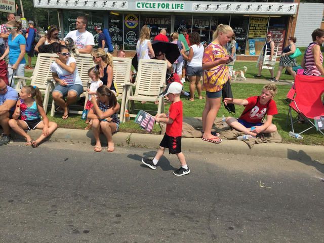Crowd seated along a street at a parade, with a child walking past in the foreground.