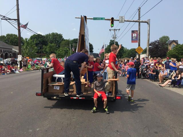 People riding on a parade float passing under an intersection traffic light, with crowds lining both sides of the street.