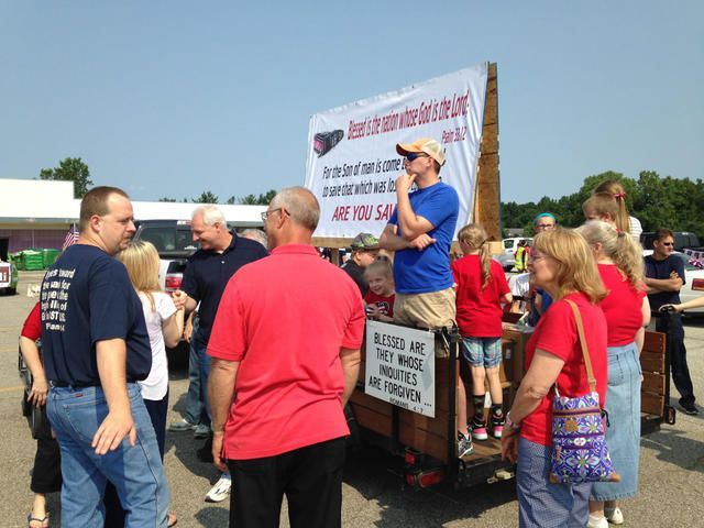 People gathered around a float with a large banner at an outdoor event